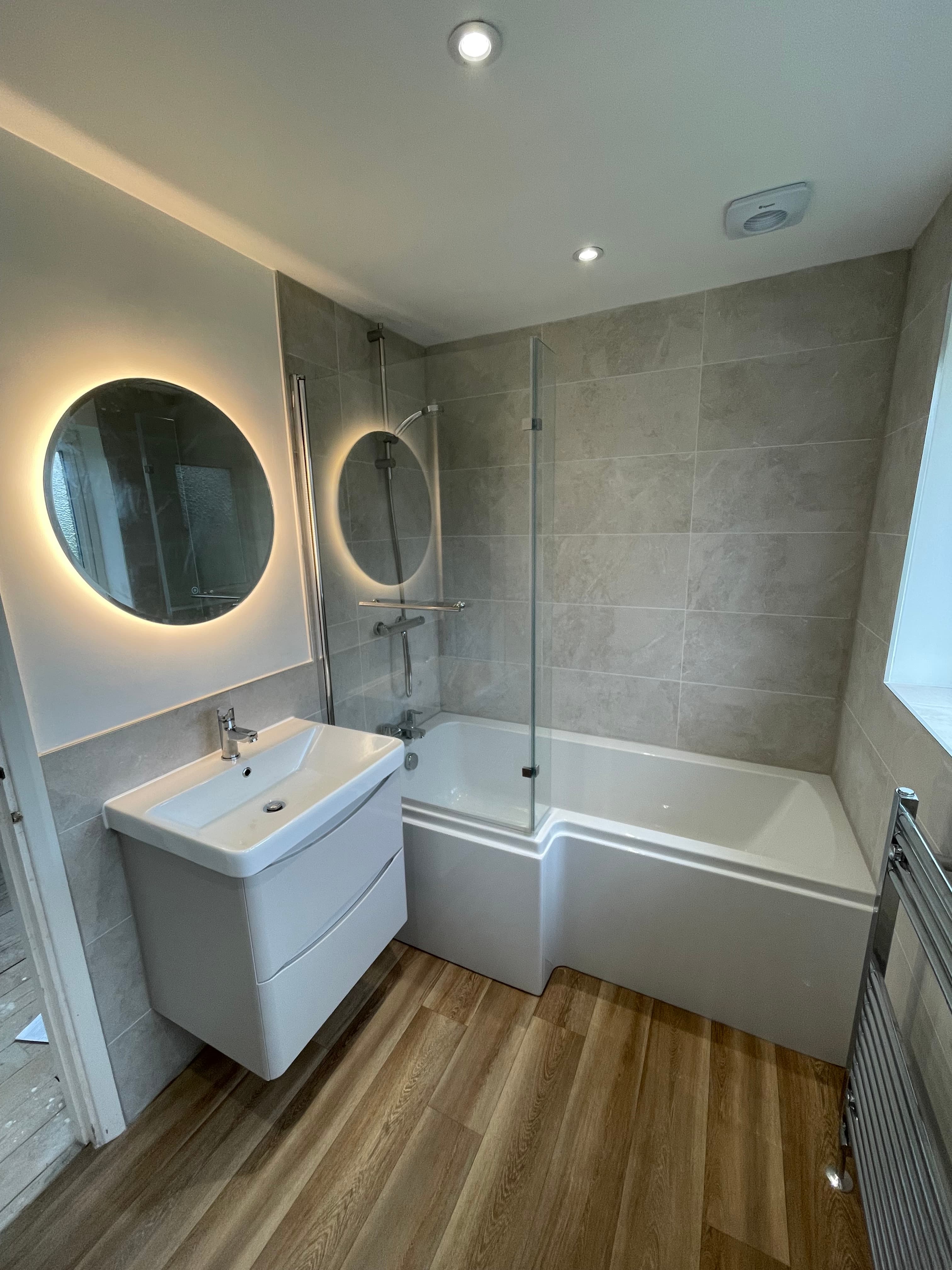 Modern bathroom installation with illuminated mirrors and glass shower screen.