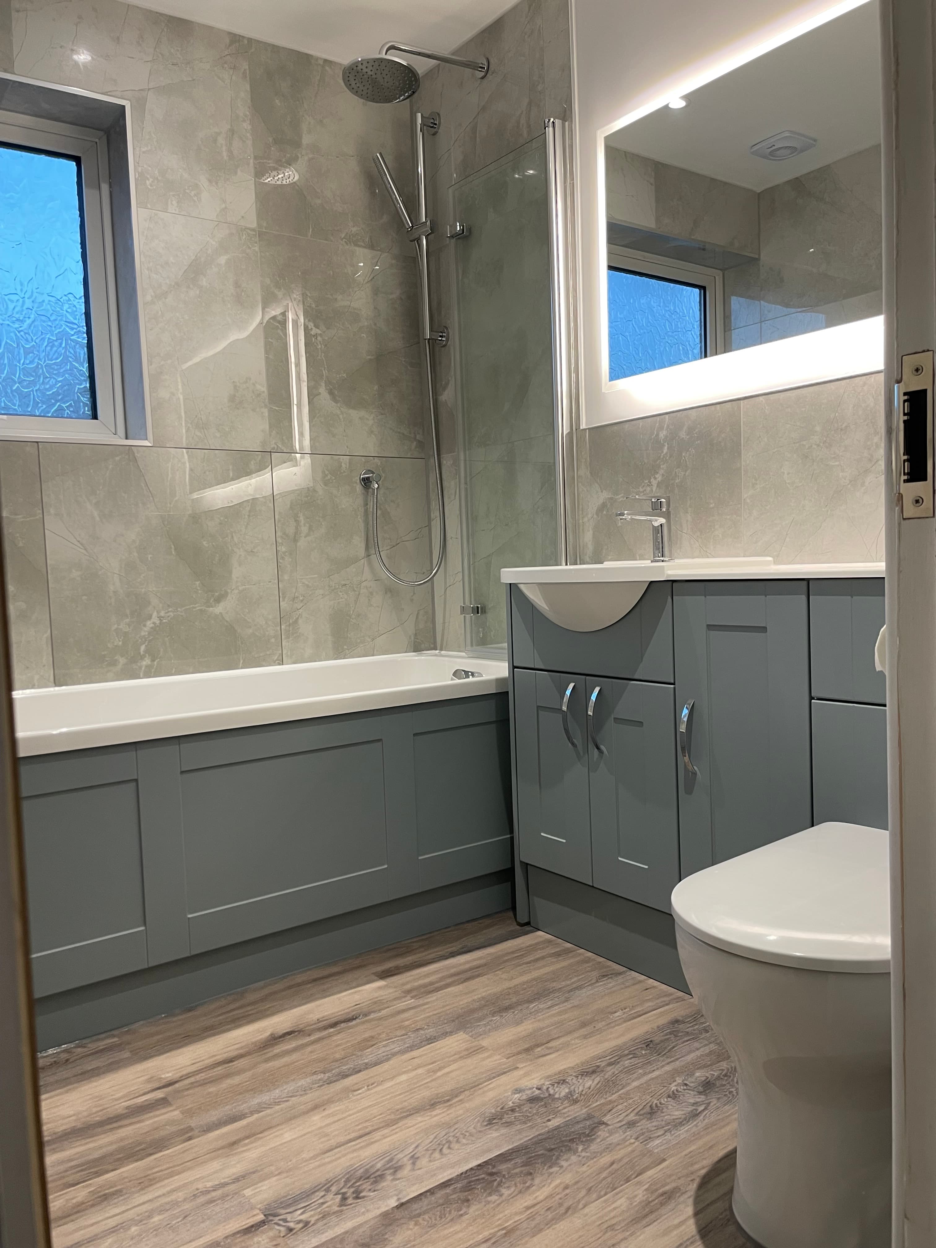 Grey bathroom renovation with shower screen, vanity unit, and tiled walls.