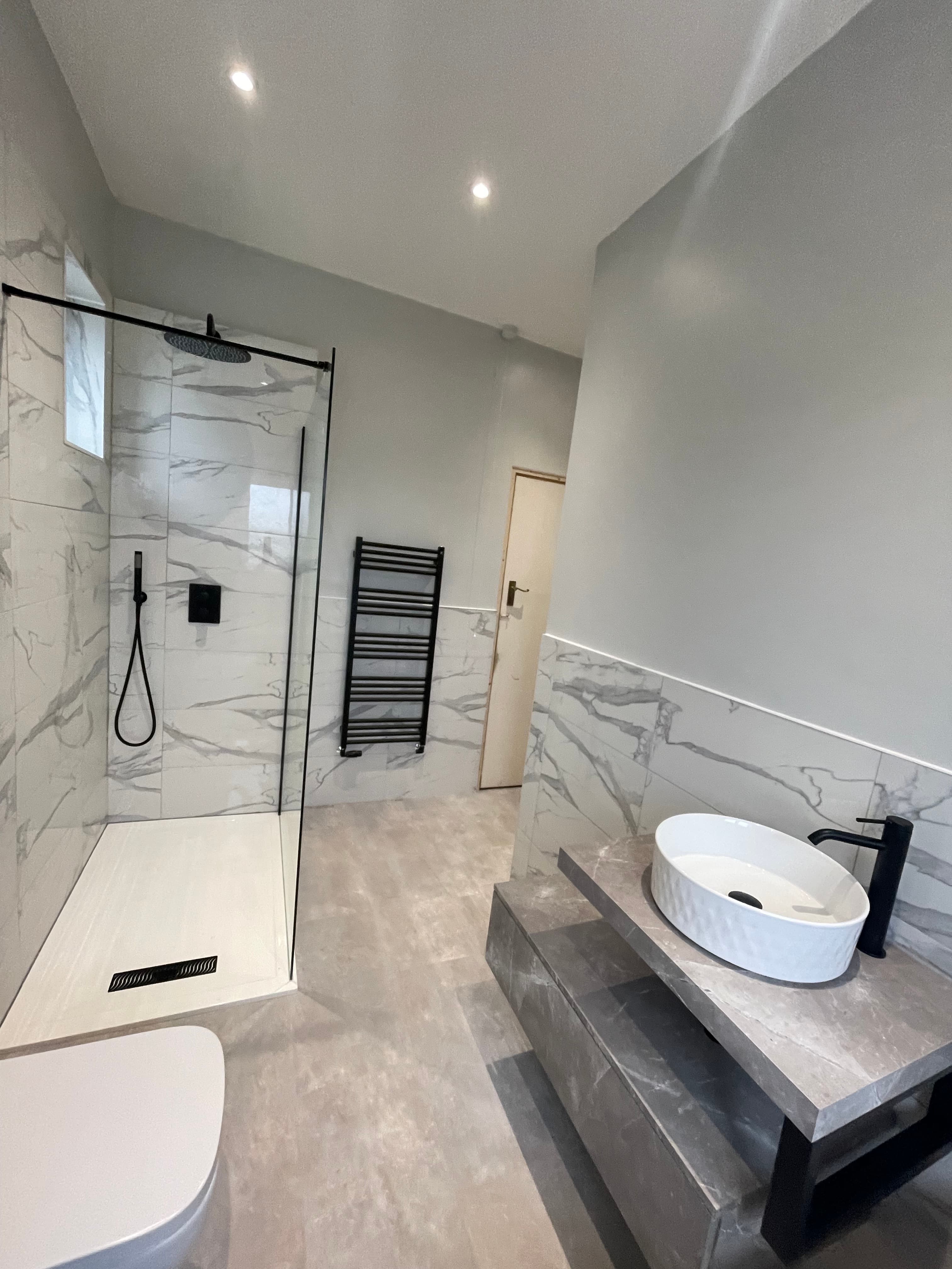 Marble-effect bathroom installation with black fixtures and walk-in shower.